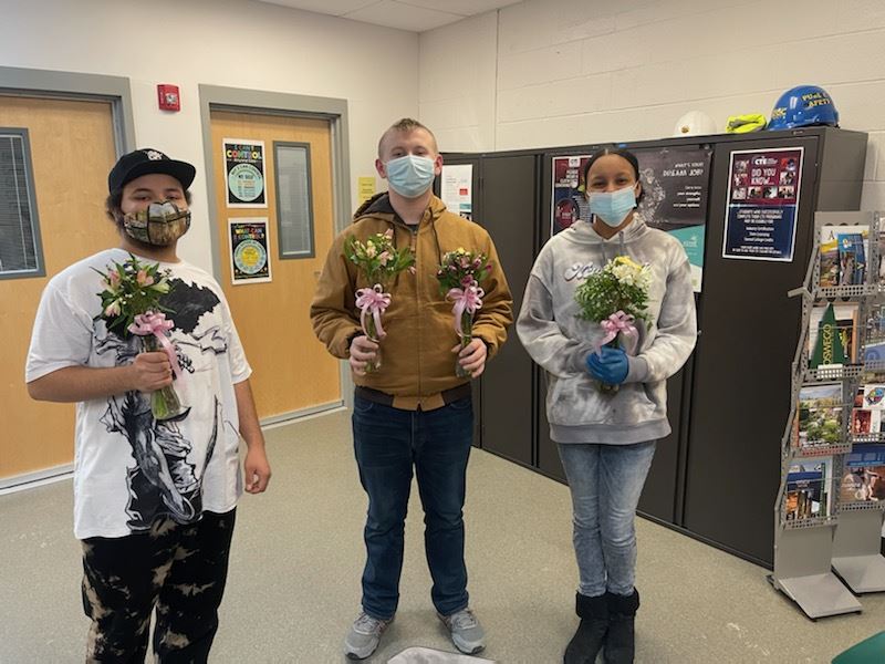 Three students carrying flowers.