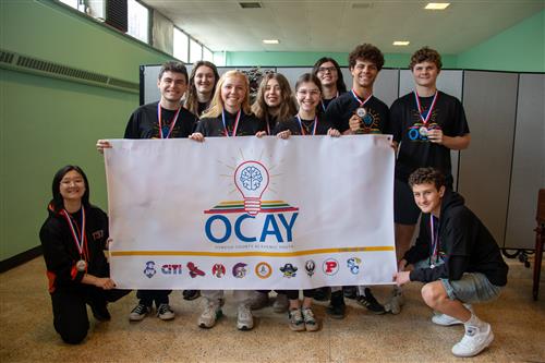 A group of students wearing medals gather around an OCAY League banner.